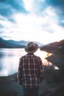 Back view of traveler in jacket in hat and shirt on stony mountains during sunset — Stock Photo