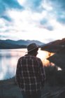 Visão traseira do viajante de jaqueta em chapéu e camisa em montanhas pedregosas durante o pôr do sol — Fotografia de Stock