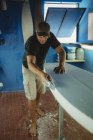 Lavoratore del legno scuoiare diligentemente tavola da surf in officina — Foto stock