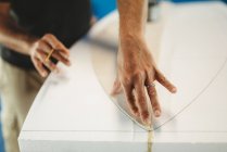 Cropped image of professional male with pencil in hand circling pattern of surf board while working in workshop — Stock Photo