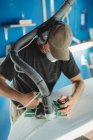 Worker in protective mask adjusting details surfboard in workshop — Stock Photo