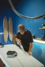 Професійний чоловік розпилює дошку під час виробництва дошки для серфінгу в невеликій майстерні з синіми стінами — стокове фото