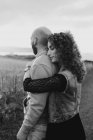 Homem abraçando por feliz encaracolado namorada em vestido e colete de ganga, enquanto de pé juntos no prado — Fotografia de Stock