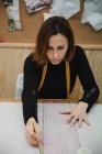 Зверху зосереджена доросла жінка сидить за столом і робить виріз під час роботи в професійній студії одягу — стокове фото