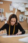 Focused adult woman sitting at table and making cutout while working in professional dressmaking studio — Stock Photo