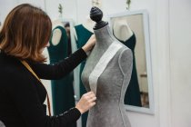Mulher com fita métrica anexando recorte de papel ao manequim com pino ao fazer roupas em oficina profissional — Fotografia de Stock