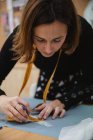 Доросла жінка використовує стрічку для вимірювання частини одягу на столі під час роботи в професійній майстерні з виготовлення одягу — стокове фото
