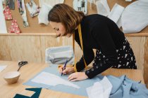 Erwachsene Frau misst Kleidungsteil auf dem Tisch mit Klebeband bei der Arbeit in professioneller Schneiderei-Werkstatt — Stockfoto