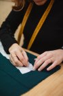 Closeup dressmaker using needle and thread to sew custom clothing over table in professional workshop — Stock Photo