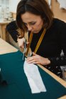 Femme utilisant des ciseaux tranchants pour couper les détails du vêtement du tissu tout en étant assis à la table dans un atelier de tailleur — Photo de stock