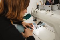 Mulher adulta sentada à mesa e fazendo peça de vestuário na máquina de costura enquanto trabalhava em estúdio profissional — Fotografia de Stock