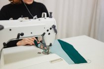 Женщина сидит за столом и делает часть одежды на швейной машине во время работы в профессиональной студии — стоковое фото