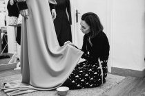 Schneiderin kniet auf Teppich und passendem Rock in maßgeschneidertem Kleid bei der Arbeit im professionellen Atelier — Stockfoto