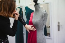 Woman using pins to attach red fabric to mannequin while making dress in professional tailor studio — Stock Photo