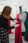 Frau mit Stecknadeln, um roten Stoff an Schaufensterpuppe zu befestigen, während sie Kleid im professionellen Schneideratelier herstellt — Stockfoto