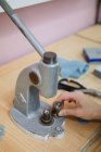 Cropped image of woman pulling lever of button maker on table in professional dressmaking workshop while making garment — Stock Photo