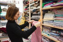 Вид сбоку на взрослую женщину, рыщущую по полке при выборе куска ткани для работы в кладовке швейной мастерской — стоковое фото