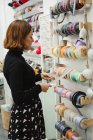 Side view of dressmaker selecting ribbons while standing near shelves in shop and buying sewing supplies — Stock Photo