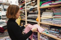 Вид сбоку на взрослую женщину, рыщущую по полке при выборе куска ткани для работы в кладовке швейной мастерской — стоковое фото