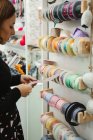 Vue latérale de la couturière sélectionnant des rubans tout en se tenant près des étagères en magasin et en achetant des fournitures de couture — Photo de stock