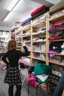 Back view of adult woman rummaging through shelf while selecting piece of cloth for work in storage room of tailor workshop — Stock Photo