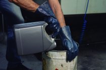 Mains gantées de l'employé masculin versant du liquide chimique de la boîte dans le baril métallique de l'usine — Photo de stock