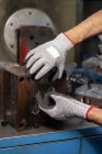Mains gantées d'homme à tout faire méconnaissable utilisant la machine sur l'usine — Photo de stock