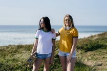 Trendy teen girls with long board in sunshine — стоковое фото