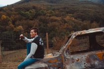 Jovem com cabelo curto segurando brilho ardente com olhos fechados enquanto sentado em um velho veículo enferrujado no campo — Fotografia de Stock