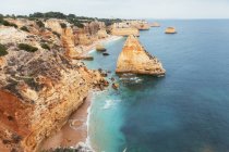 Чистое синее море, размахивающее у грубых скалистых скал в безоблачный день в Португалии — стоковое фото