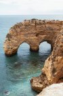 Волна чистой морской воды возле дуги грубого утеса в спокойный день в Португалии — стоковое фото