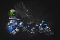 Vista dall'alto di bottiglie di plastica e scatole disposte su una superficie di sfondo scuro — Foto stock