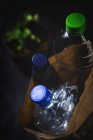 De dessus sac en papier sale avec des bouteilles en plastique jetées placées sur fond noir — Photo de stock