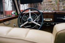 Вид на черное металлическое рулевое колесо и приборную панель с передними бежевыми сиденьями классического автомобиля — стоковое фото