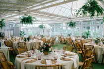 Big spacious room with festive decorated tables and wooden chairs under ceiling with green plants — Stock Photo