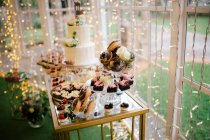 Festive decorated sweet cakes muffins and white flowered cake on stand in restaurant — Stock Photo