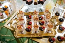 Dall'alto decorato dolce buonissimo cheesecake tiratori su vassoio d'oro e torta fiorita rosa su bancarella di vetro in ristorante — Foto stock