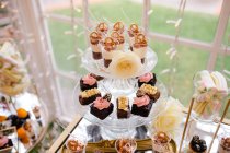 De cima doce deliciosos bolos de chocolate cremoso decorados com flores em suporte de vidro no café — Fotografia de Stock
