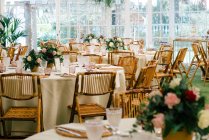 Grande chambre spacieuse avec tables décorées festives et chaises en bois sous plafond avec des plantes vertes — Photo de stock