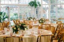 Grande chambre spacieuse avec tables décorées festives et chaises en bois sous plafond avec des plantes vertes — Photo de stock