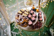 Сверху сладкие вкусные сливочные шоколадные торты, украшенные цветами на стеклянном стенде в кафе — стоковое фото