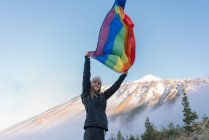 Человек на вершине горы размахивает флагом ЛГБТ — стоковое фото