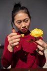 Азійка розриває пелюстку з жовтої троянди. — стокове фото