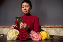 Jovem mulher asiática sentada na loja e trabalhando com rosas — Fotografia de Stock