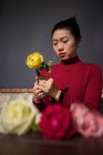 Junge asiatische Frau sitzt im Geschäft und arbeitet mit Rosen — Stockfoto