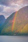 Таинственный пейзаж красочной радуги в скалистых горах в спокойной воде под облачным небом в Норвегии — стоковое фото