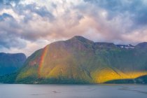 Mysterious landscape of colorful rainbow in rocky mountains in calm water under cloudy sky in Norway — Stock Photo