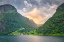 Paisagem deslumbrante em água verde refletindo céu nublado lavar montanhas rochosas com árvore verde e grama na Noruega — Fotografia de Stock