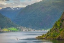 Boat in stunning landscape on green water reflecting cloudy sky washing rocky mountains with green tree and grass in Norway — Stock Photo