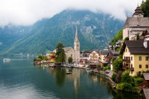 Estanque limpio con agua tranquila y casas encantadoras de la pequeña ciudad situada cerca de la cresta de la montaña en el día nublado en Austria - foto de stock